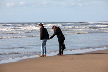 Katwijk, Hollanda - 23 Nisan 2017: Bir kadın ve bir adam Katwijk plaj boyunca güneşli bir günde yürüyor. Hollanda