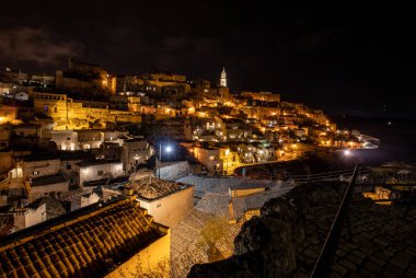 Matera 'daki antik Sassi bölgesinde geceleri, antik mağara evleri ile tanınan şaşırtıcı aydınlık binalar. Basilicata. İtalya