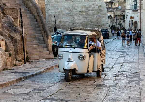 Matera, İtalya - 15 Eylül 2019: Matera şehrinde tarihi bir bölge olan Sassi di Matera 'da bir turist taksisi olarak kullanılan Piaggio Ape Calessino üzerinde turistler, antik mağara evleri ile tanınırlar. Basilicata. İtalya