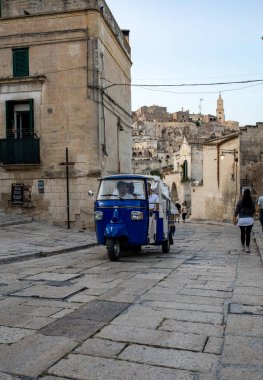 Matera, İtalya - 18 Eylül 2019: Matera şehrinde tarihi bir bölge olan Sassi di Matera 'da bir turist taksisi olarak kullanılan Piaggio Ape Calessino üzerinde turistler, antik mağara evleri ile tanınırlar. Basilicata. İtalya