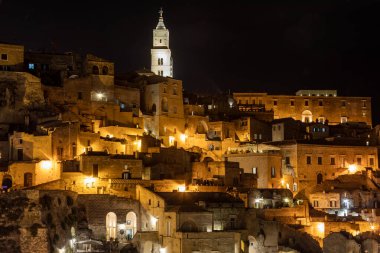 Matera 'nın antik taş şehir merkezinde, arka planda aydınlatmalı kule katedrali olan bir caddenin güzel gece manzarası. Bazilika. İtalya