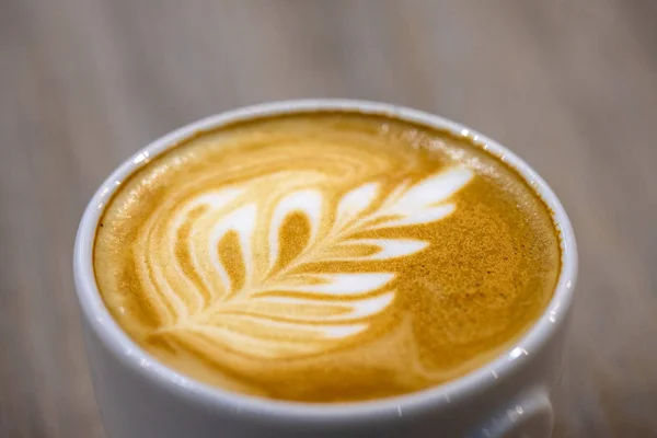 The coffee barista poured milk into the coffee and created a beautiful leaf.