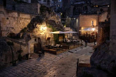 Matera, İtalya - 14 Eylül 2019: Matera, İtalya 'nın akşam manzarası, Sassi di Matera şehrinin tarihi bir bölgesi olan Sassi di Matera' daki kaldırım kafelerinin avlularını aydınlatan renkli ışıklarla. Basilicata. İtalya