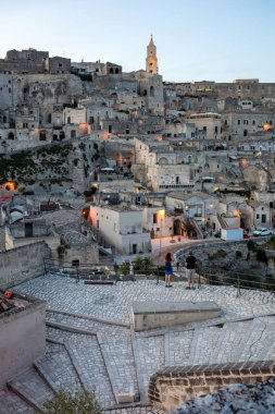 Matera; İtalya - 15 Eylül 2019: Matera şehrinin akşam manzarası; Matera şehrinin tarihi bir bölgesi olan Sassi di Matera 'daki eski binaların renkli ışıklarıyla. Basilicata. İtalya