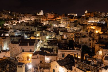 Matera 'daki antik Sassi bölgesinde geceleri, antik mağara evleri ile tanınan şaşırtıcı aydınlık binalar. Basilicata. İtalya