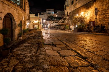 Matera, İtalya - 19 Eylül 2019: Matera, İtalya 'nın akşam manzarası, Sassi di Matera şehrinin tarihi bir bölgesi olan Sassi di Matera' daki kaldırım kafelerinin avlularını aydınlatan renkli ışıklarla. Basilicata. İtalya
