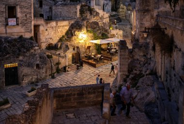 Matera, İtalya - 14 Eylül 2019: Matera, İtalya 'nın akşam manzarası, Sassi di Matera şehrinin tarihi bir bölgesi olan Sassi di Matera' daki kaldırım kafelerinin avlularını aydınlatan renkli ışıklarla. Basilicata. İtalya