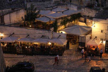 Matera, İtalya - 14 Eylül 2019: Matera, İtalya 'nın akşam manzarası, Sassi di Matera şehrinin tarihi bir bölgesi olan Sassi di Matera' daki kaldırım kafelerinin avlularını aydınlatan renkli ışıklarla. Basilicata. İtalya