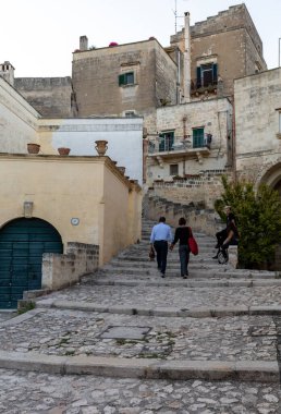 Matera, İtalya - 14 Eylül 2019: Matera şehrinin tarihi bir bölgesi olan Sassi di Matera 'daki Cobblestone caddesinde yürüyüş yapan çift. Basilicata. İtalya