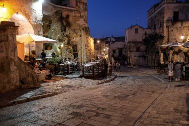Matera, İtalya - 14 Eylül 2019: Matera, İtalya 'nın akşam manzarası, Sassi di Matera şehrinin tarihi bir bölgesi olan Sassi di Matera' daki kaldırım kafelerinin avlularını aydınlatan renkli ışıklarla. Basilicata. İtalya
