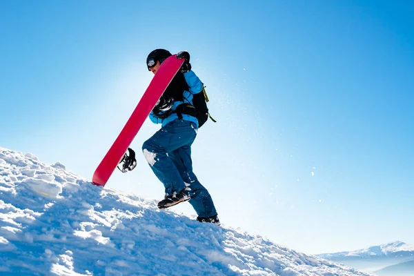 Snowboarder Grimper avec Red Snowboard dans les montagnes à la journée ensoleillée. Snowboard et sports d'hiver — Photo