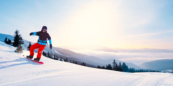 Ung snowboardåkare Ridning röd snowboard i bergen på soliga dagen. Snowboard och vintersport — Stockfoto