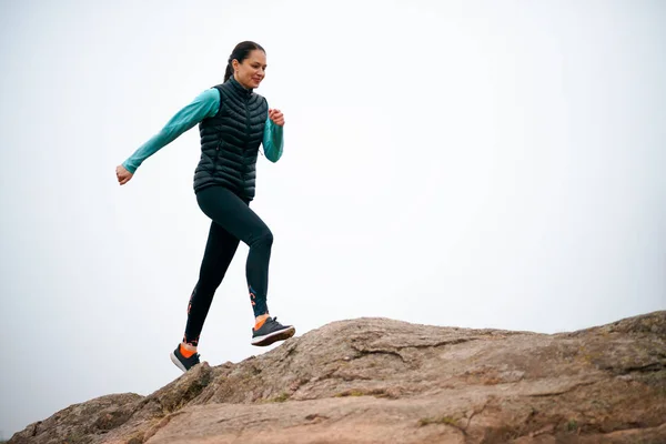 Krásná usměvavá žena běžící po horské stezce na chladném podzimním večeru. Sport a aktivní životní styl. — Stock fotografie