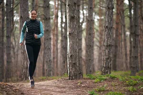 Mulher sorridente bonita que corre na trilha da floresta na noite fria do outono. Desporto e Estilo de Vida Ativo . — Fotografia de Stock