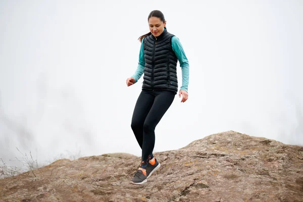 Hermosa mujer sonriente corriendo en el sendero de la montaña en la fría noche de otoño. Deporte y estilo de vida activo . — Foto de Stock