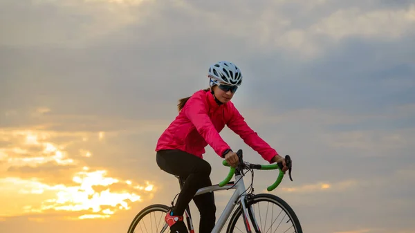 Junge Radfahrerin auf Rennrad bei Sonnenuntergang. gesunder Lebensstil und Outdoor-Sportkonzept — Stockfoto