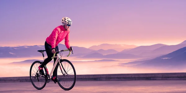 紫の夕日の美しい山の中で若い女性サイクリスト乗馬ロードバイク.冒険,健康的なライフスタイル,スポーツ — ストック写真