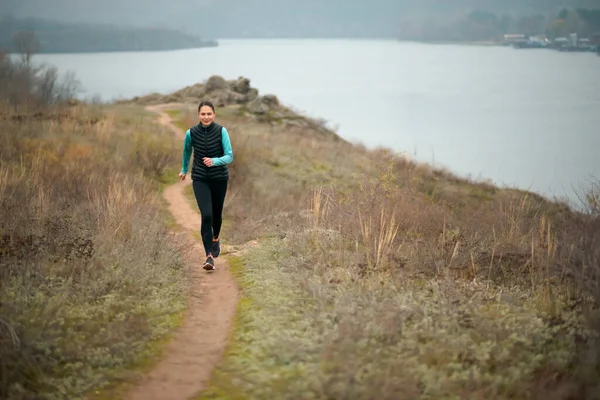 Hermosa mujer sonriente corriendo en el sendero de la montaña en la fría noche de otoño. Deporte y estilo de vida activo . —  Fotos de Stock