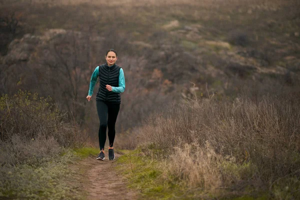 Krásná usměvavá žena běžící po horské stezce na chladném podzimním večeru. Sport a aktivní životní styl. — Stock fotografie