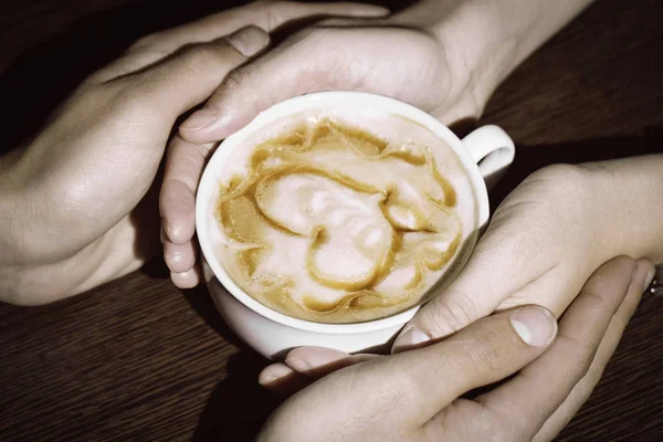 Quatro mãos enroladas em torno de uma xícara de café com desenho do coração — Fotografia de Stock