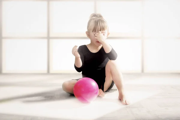 A frustrated little gymnast is sitting with the ball.