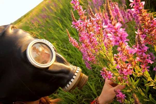 Vrouw met gasmasker op zoek roze bloemen — Stockfoto
