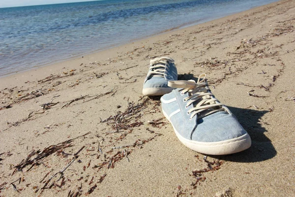 Old blue sneaker on beach. Travel concept. Stock Photo