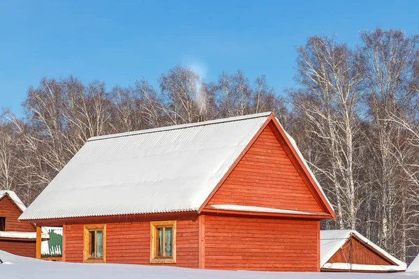 Altai bölgesindeki mavi gökyüzüne karşı turist üssünde karla kaplı çatısı olan güzel bir ev.