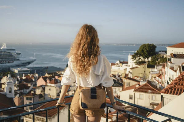 Blonde woman standing on the balcony and looking at coast view