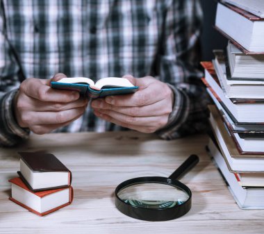 Kütüphanede büyük kitaplar arasında minyatür kitap okurken erkek