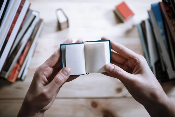 A man reading a miniature book among the big books in the library — Stock Photo, Image