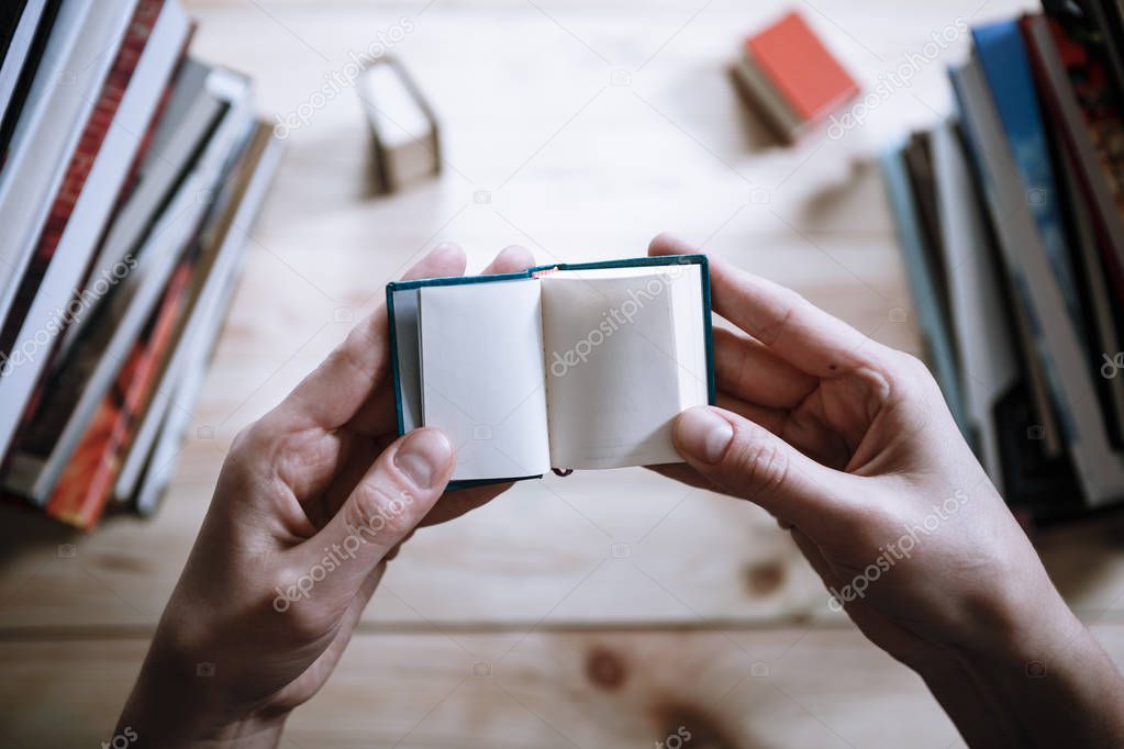 A man reading a miniature book among the big books in the library