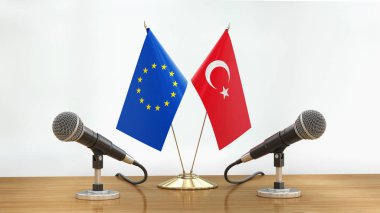 Mikrofonlar ve bayraklar, odaklanmamış arka planda bir masanın üzerinde.