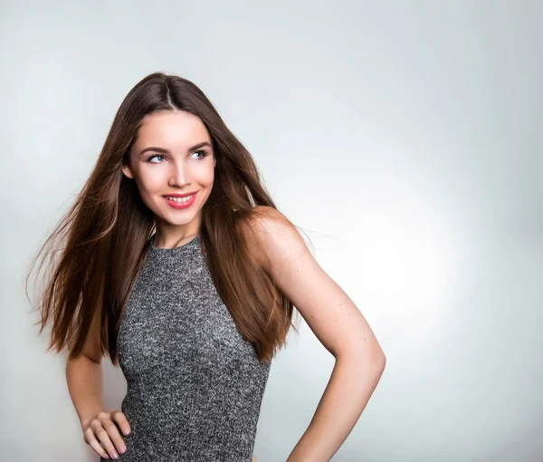 uzun kahverengi saçlı neşeyle gri arka plan üzerinde poz gülümseyen güzel genç kadın