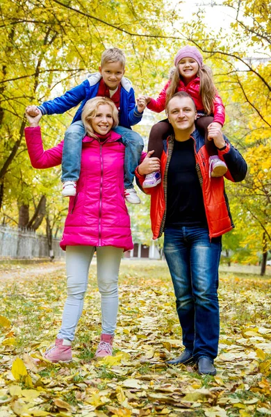 Děti, které sedí na ramenou rodičů na podzim — Stock fotografie