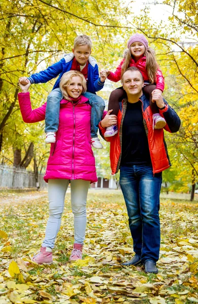 Niños sentados sobre los hombros de los padres en otoño —  Fotos de Stock