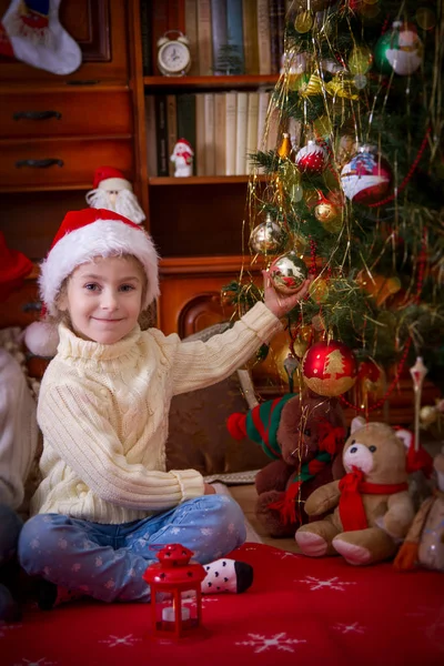 Menina sentada sob a árvore de Natal segurando bola — Fotografia de Stock