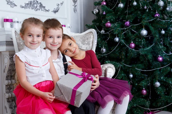 ギフト ボックスとマゼンタのクリスマス ツリーの下に座って子供たち — ストック写真