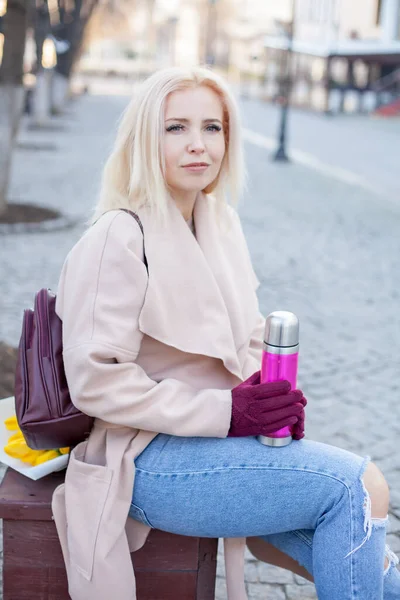 エレガントなコートと手袋でブロンドの髪を持つ豪華な女性の屋外熱いお茶の魔法瓶と路上に座って — ストック写真