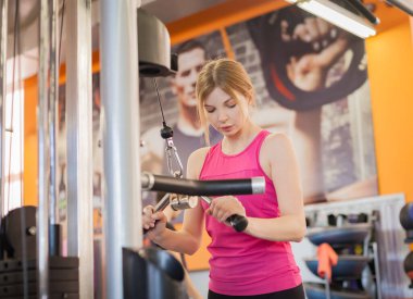 Kadın vücut geliştirme eğitimi alıyor. Uzatma makinesiyle ağırlık kaldırıyor.