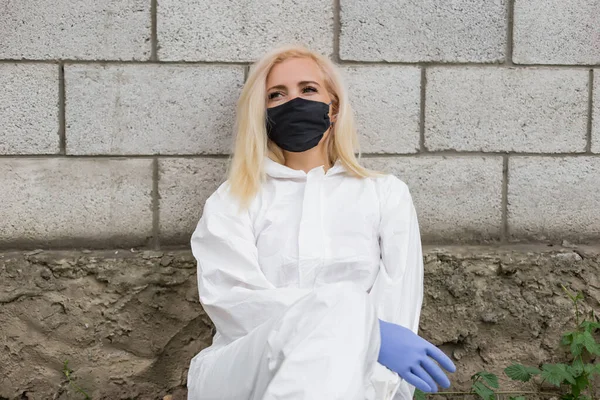 Женщина Черной Маске Белый Защитный Костюм Перчатки Сидящие Стены — стоковое фото