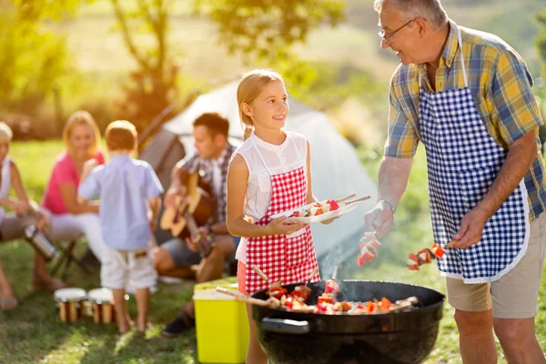 Bunicul zâmbitor dând carne nepoatei la grătar — Fotografie, imagine de stoc