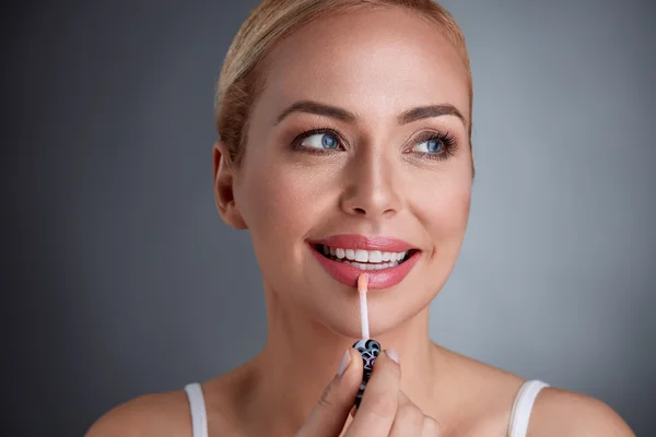 Mujer sonriente aplicando brillo de labios en los labios —  Fotos de Stock