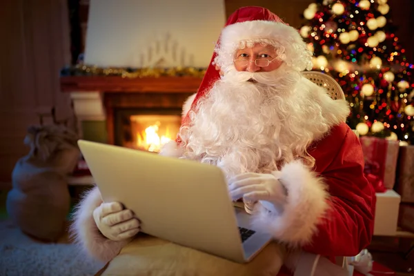 Jultomten som sitter vid den öppna spisen med laptop — Stockfoto