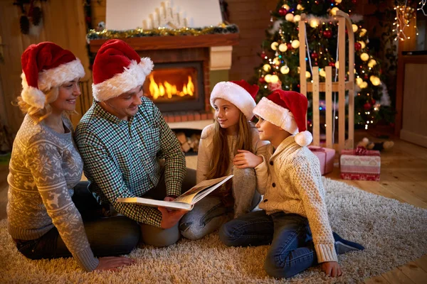 Eltern und Kinder lesen an Heiligabend am Kamin ein Buch — Stockfoto