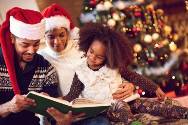 Anne, baba ve kızı Noel'de şömine, bir kitap okumak