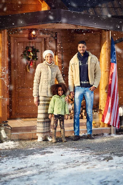 Junge Familie vor Holzhaus an einem Wintertag — Stockfoto