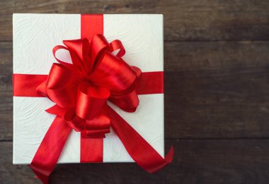 ahşap masa üzerinde kırmızı fiyonklu hediye kutusu