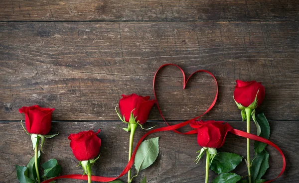 Rosas rojas y cinta en forma de corazón sobre mesa de madera —  Fotos de Stock