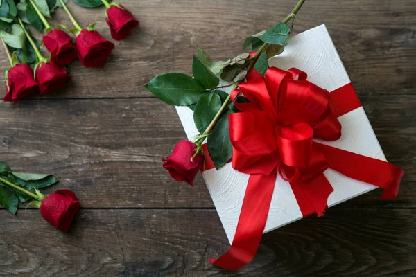 Rose rosse e confezione regalo su tavolo in legno — Foto Stock